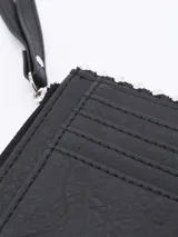 Billetera plateada rectangular con cierre de cremallera y correa de mano. Decorada con tachas redondas plateadas en los bordes.