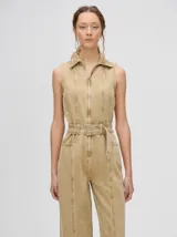 Mono largo de denim azul con corte holgado, recto en las piernas y entallado en el tronco. Tiene cuello camisero, cierre frontal con cremallera y cinturón ajustable.