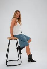 Bermuda de jean de tiro medio, con corte recto y largo por encima de la rodilla. Presenta un diseño clásico de cinco bolsillos, cierre frontal con botón y costuras reforzadas en tono contrastante.