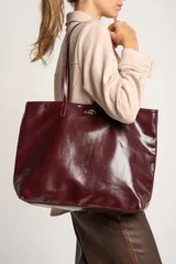 Bolso tipo tote de gran tamaño en color bordó con acabado brillante. Cuenta con doble asa de hombro y placa metálica decorativa con logo en la parte frontal.