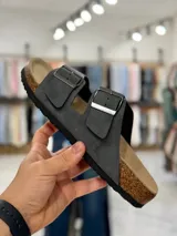 Sandalias de dos tiras negras con hebillas metálicas ajustables, plantilla anatómica y suela plana.