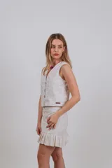 Chaleco sastrero de diseño estructurado, confeccionado en tela blanca con sutiles bordados florales en tonos dorados y crudos. Presenta escote en V, cierre frontal con botones y corte a la cintura.