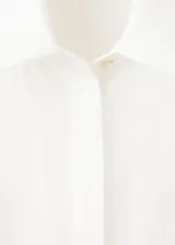Vestido midi camisero de lino color blanco, sin mangas, con cuello solapa, cierre frontal de botones y cinturón ajustable del mismo género. Cuenta con detalles de costura calada en el frente.