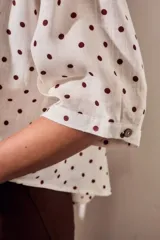 Blusa de lino y viscosa color blanco con estampado de lunares marrones, de manga corta y cuello camisero con cierre frontal de botones.