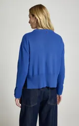 Sweater de punto color azul, de corte recto y ligero estilo holgado, con cuello redondo, mangas largas con puños ajustados por botones metálicos y dobladillo acanalado.