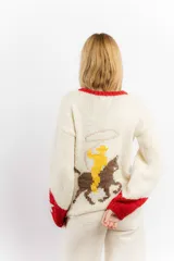 Sweater tejido a mano en lana merino color crudo, con cuello y puños en rojo. Presenta un diseño con motivos de un cowboy y estrellas.