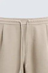 Bermuda negra de corte recto, con cintura elástica ajustable mediante cordón, pliegues frontales y bolsillos de vivo en la espalda. El bajo tiene un dobladillo vuelto.