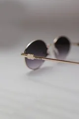 Lentes de sol con montura metálica dorada y cristales ovalados con degradé de gris a transparente.