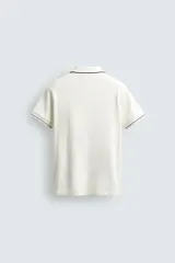 Remera polo de punto canalé color azul marino, de corte regular fit, con cuello solapa y cierre frontal de botones a presión. Cuenta con mangas cortas con ribetes blancos en los bordes del cuello y de las mangas.