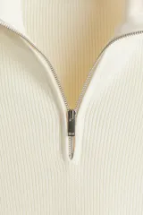 Buzo de punto color crema, con cuello alto y medio cierre metálico. Presenta un tejido acanalado en el cuello y un calce regular.