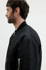 Campera bomber negra, ligeramente acolchada, confeccionada en nylon. Presenta cuello elevado acanalado, cierre frontal, bolsillos al bies con botón a presión oculto, bolsillo con cierre en una manga y dos bolsillos interiores con botón a presión. Los puños y el bajo son de remate acanalado ancho.