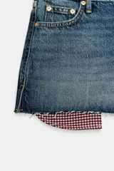 Shorts de jean tiro medio, corte mom fit, con bajo deshilachado y forro de bolsillos delanteros estampado a cuadros que asoma por debajo.