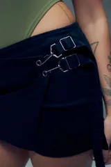 Short pollera de algodón en color negro, con diseño de falda cruzada y detalle de hebillas metálicas en la cintura. Cuenta con cierre posterior.
