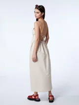 Vestido largo blanco de algodón con escote en V, breteles finos regulables y espalda descubierta con lazo para atar. Presenta un diseño holgado con bolsillos laterales.