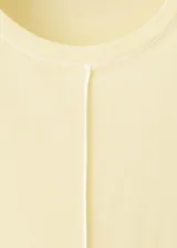 Remera de algodón color amarillo claro, con cuello redondo, manga corta y costuras pespunteadas a la vista en el frente y sisas.