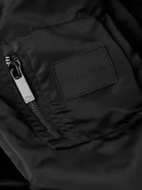 Campera bomber negra Calvin Klein de satén de nailon reciclado, con cuello, puños y bajo de punto de canalé. Tiene cierre de cremallera, bolsillos de hendidura en la cintura, detalle de cremallera en la manga e insignia con el logo de goma de Calvin Klein en la manga. El forro y el relleno son de poliéster reciclado REPREVE®.