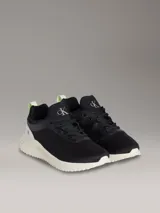 Zapatillas tipo runner Calvin Klein en color negro con suela de EVA blanca y detalles en verde claro en el talón. Presentan diseño tipo calcetín, parte superior de malla técnica y logo de la marca en la lengüeta y el lateral.