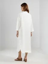 Camisa larga celeste confeccionada en lino, con cuello clásico, mangas 3/4, silueta fluida, dobladillo curvado en las costuras laterales y bolsillos discretos.