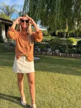 Camisa color marrón claro confeccionada en lino metalizado, con volados en el frente y cuello, mangas largas y botones ocultos. Corte holgado, más larga en la parte trasera.