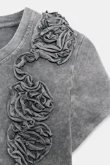 Camiseta de algodón con efecto lavado, cuello redondo y manga corta. Presenta un detalle decorativo de flores en relieve confeccionadas en el mismo tejido sobre el lado izquierdo del pecho.