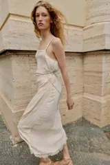 Vestido midi lencero de color blanco, confeccionado en tejido con efecto arrugado. Cuenta con escote recto, tirantes finos ajustables, diseño cruzado con cinturón fino para anudar y detalles de encaje en los acabados de la falda.
