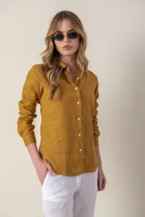 Camisa de lino color mostaza con cuello clásico, cierre frontal de botones y mangas largas con puños abotonados. Presenta un pequeño bordado distintivo en el ruedo inferior.