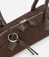 Cartera tipo shoulder bag de tamaño pequeño y formato alargado, confeccionada en material sintético efecto gamuza. Cuenta con asas de hombro estructuradas, cierre superior con cremallera y detalles metálicos decorativos.