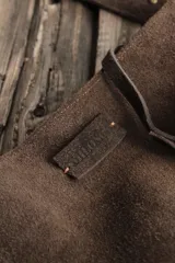 Bandolera confeccionada en cuero de gamuza marrón, con cierre superior. Presenta un llavero colgante con forma de estrella revestido en tachas metálicas y tiras flecadas en tono dorado.