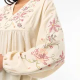 Blusa de color beige con cuello en V, mangas largas abullonadas con puños elásticos y bordados florales en el pecho y las mangas.