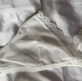 Conjunto de lencería de dos piezas color blanco, confeccionado en tela suave y semitransparente con detalles de encaje en los bordes. Incluye un bralette triangular sin aro ni relleno, con breteles regulables y una bombacha vedetina a juego.