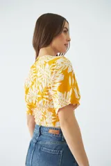 Blusa estampada con diseño de hojas en color amarillo y blanco, con escote en V cruzado, mangas cortas y elástico en la cintura.