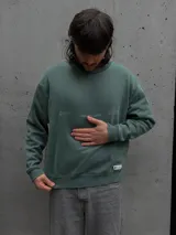 Buzo de cuello redondo color verde, con estampado gráfico minimalista en el pecho y etiqueta pequeña en el ruedo.
