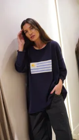 Sweater de hilo de algodón color azul marino, con cuello redondo y manga larga. Presenta un diseño tejido de la bandera de Uruguay en el frente.