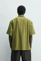 Camisa de corte relajado confeccionada en tejido fluido de lyocell y viscosa, color verde oliva. Presenta cuello solapa, manga corta, cierre frontal de botones y dos bolsillos plastrón en la parte inferior.