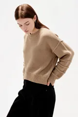Sweater de punto canalé color beige, de corte holgado, con cuello redondo a la base y mangas largas con costuras decorativas.