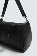 Bolso de viaje negro con textura grabada, compartimento principal con cierre de cremallera, bolsillo interior con cremallera, bolsillo frontal con cremallera, tres asas de mano (una lateral) y asa de hombro ajustable y extraíble.