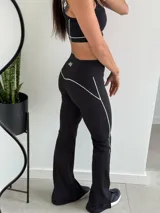 Conjunto deportivo compuesto por un top de breteles finos con logo estampado y un pantalón largo de corte acampanado con aberturas laterales en el bajo. Ambas prendas son de color negro con detalles de costuras blancas a contraste.
