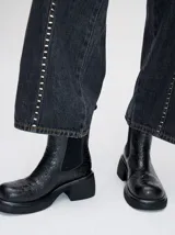 Bota tipo Chelsea de caña media, confeccionada en cuero vacuno negro con acabado mate. Presenta paneles laterales elásticos, tirador trasero y una suela robusta con plataforma delantera y taco cuadrado.