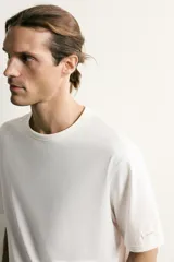 Camiseta relaxed fit color blanco, de cuello redondo y manga corta. Presenta un pequeño parche aplicado a contraste en el extremo de la manga y terminaciones en rib.