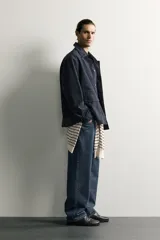 Sobrecamisa regular fit confeccionada en tejido de algodón negro con estructura canvas. Tiene cuello solapa, manga larga con puño abotonado, bolsillos de plastrón con solapa en la cadera y un bolsillo en el pecho. Cierre frontal con botones ocultos bajo solapa.