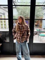 Campera reversible de corte holgado con cuello alto. De un lado presenta un diseño a cuadros en tonos marrones y beige, y del otro lado un diseño liso. Cuenta con cierre frontal de botones y mangas largas.
