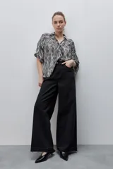 Jean wide leg negro de tiro alto, confeccionado en denim rígido, con diseño de cinco bolsillos, presillas para cinto, cierre frontal con botón y ruedo desflecado.