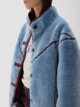 Campera de pelo sintético en color azul, con cuello alto y cierre frontal de botones. Presenta detalles de terminación en cuero vegano color bordó en los bordes, costuras y solapas.