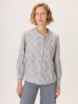 Camisa de algodón color gris claro, con cuello mao, cierre frontal de botones y mangas largas. Presenta un estampado sutil de hojas y flores, y detalles de bordado calado en los hombros.