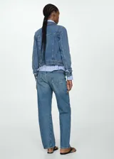 Chaqueta vaquera de corte ajustado y diseño corto, confeccionada en tejido de algodón estilo denim. Cuenta con cuello camisero de solapa, cierre frontal de botones metálicos, bolsillos de parche con solapa en el pecho y manga larga con puños abotonados.