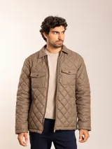 Campera marrón con diseño acolchado a rombos, cuello camisero de pana y cierre frontal con cremallera. Tiene dos bolsillos de parche en el pecho con botón a presión y dos bolsillos laterales.