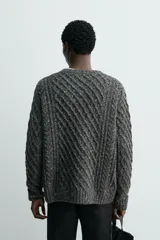 Jersey de punto con diseño de trenzas diagonales, confeccionado en lana con efecto moteado. Presenta cuello redondo, manga larga y terminaciones en rib.
