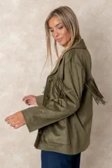 Chaqueta de gamuza sintética color marrón, con diseño de flecos en el pecho y la espalda. Presenta cierre frontal con botones, cuello camisero y bolsillos cuadrados frontales.