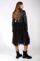 Chaqueta de cuero sintético negra con cierre frontal, solapas y cinturón integrado, combinada con una falda de tul con volados en capas.