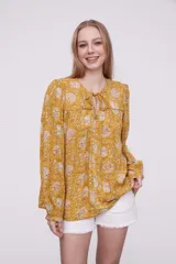 Blusa color mostaza con estampado floral, cuello redondo con lazo, mangas largas con puños elásticos y corte holgado.